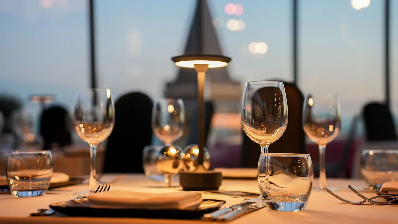 A set table with a lamp and wine glasses at dusk, Saint Antoine Church softly in the background