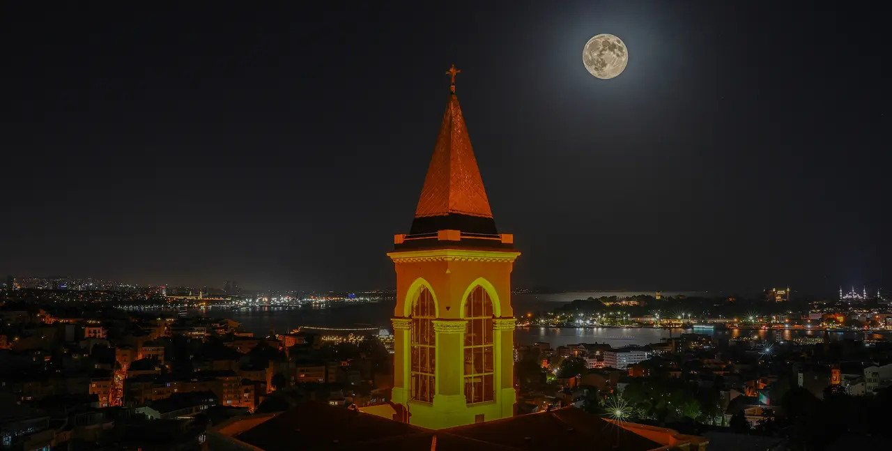 A full moon over the illuminated bell tower of Saint Antoine Church and the Istanbul skyline, seen from 360 Istanbul